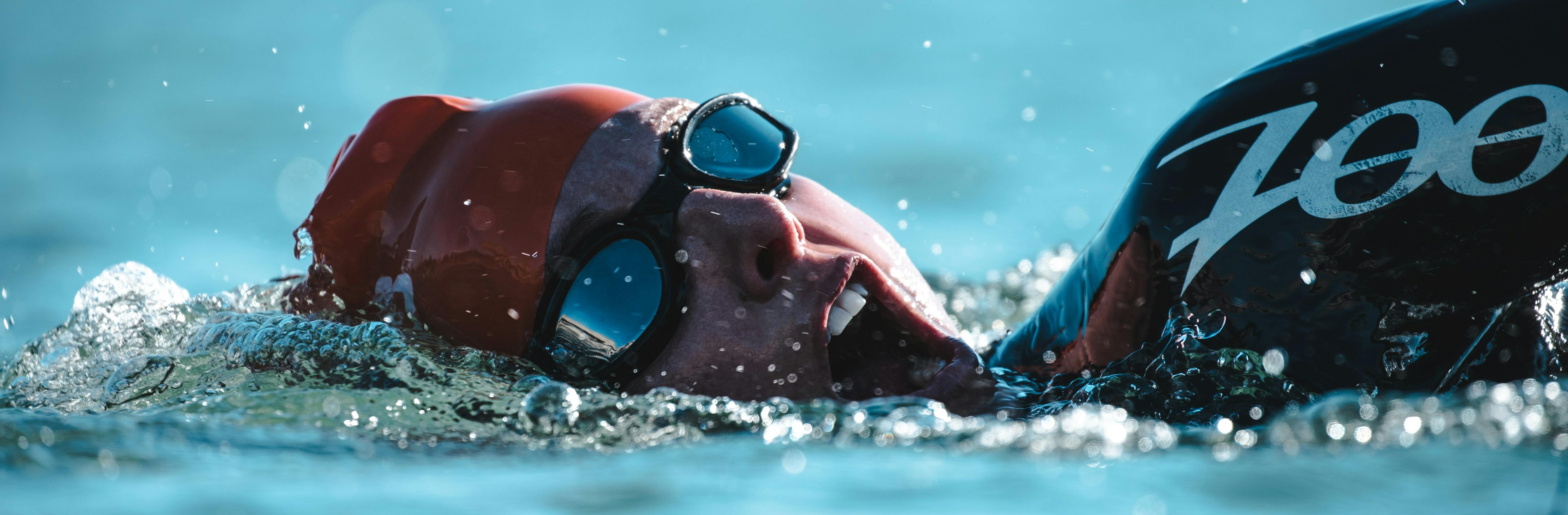 An open water swimmer in red swim cap and goggles