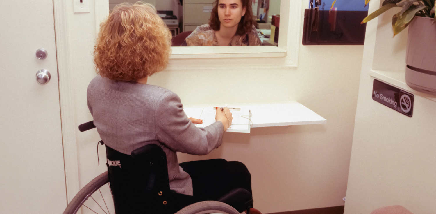 A woman in a wheelchair talking to a female receptionist