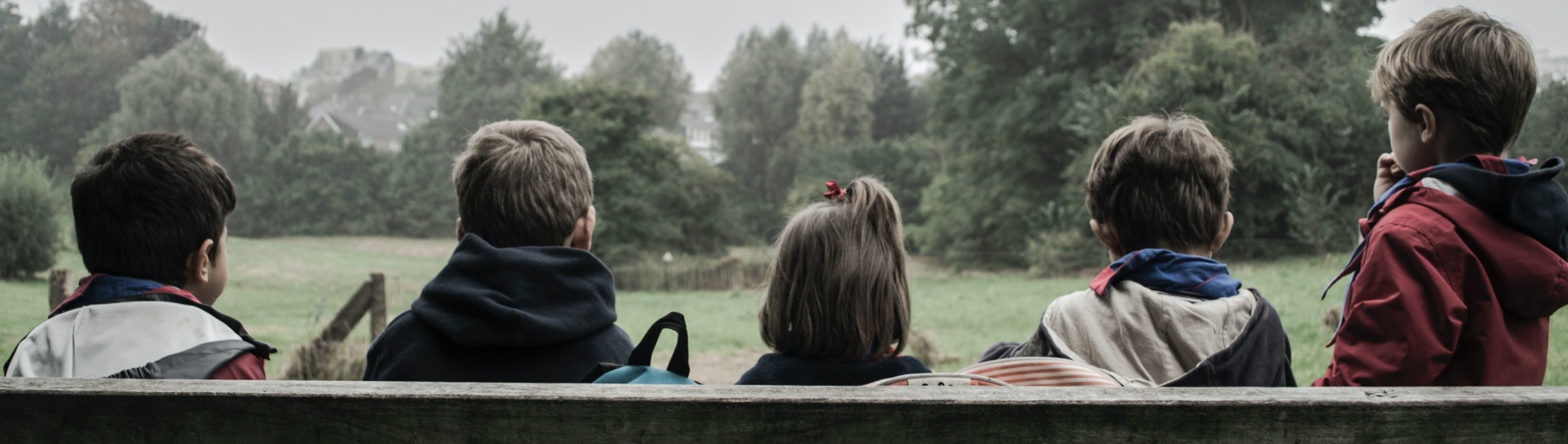 Children sitting on a bench overlooking grass and trees