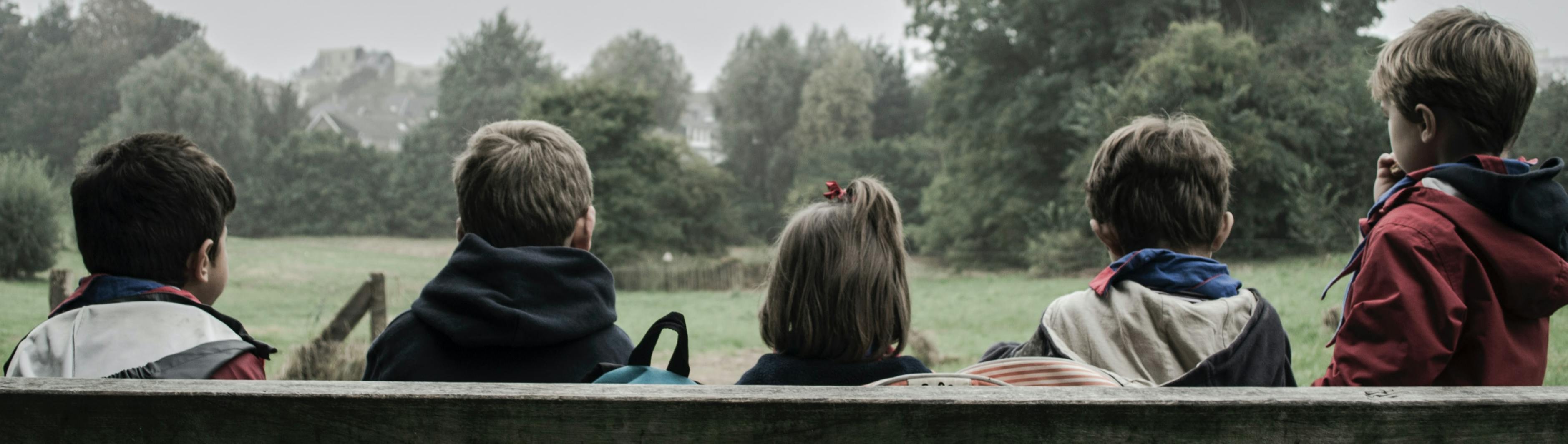 Children sitting on a bench overlooking grass and trees