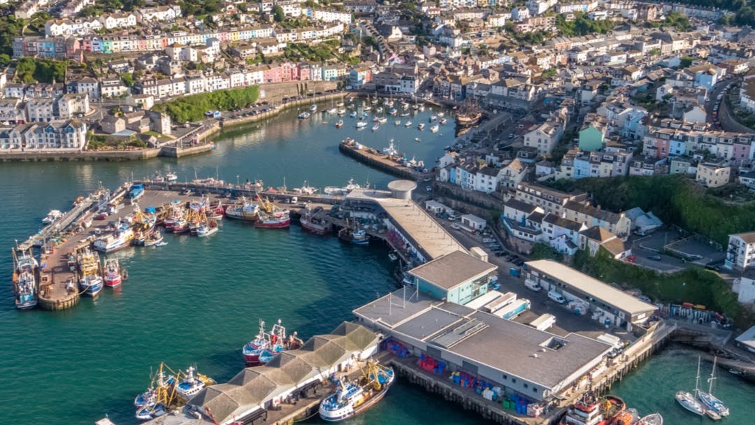 Aerial view of Brixham showing the fish market with trawler boats moored up, the inner Harbour & residential areas around it