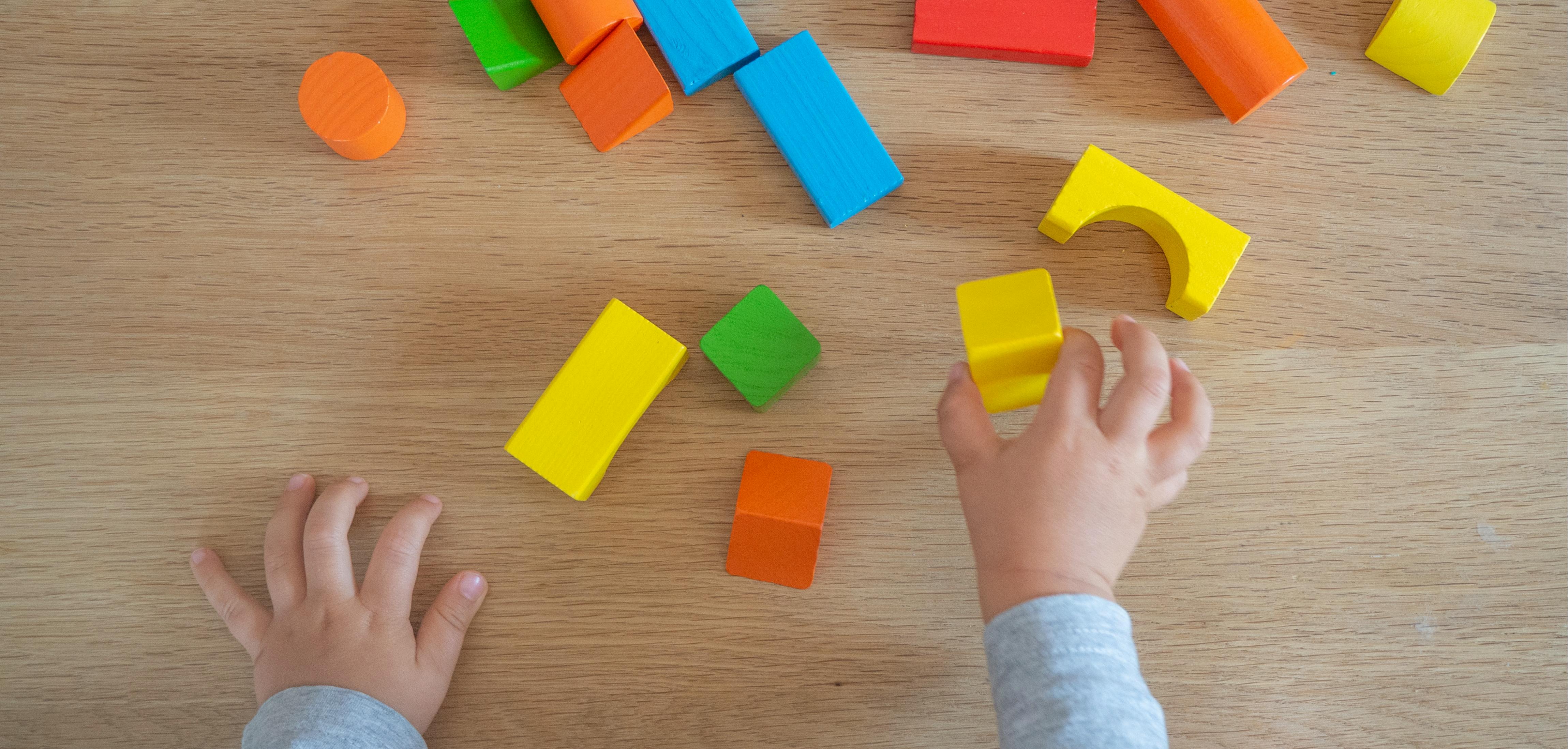 A toddler plays with coloured bricks on a wooden floor
