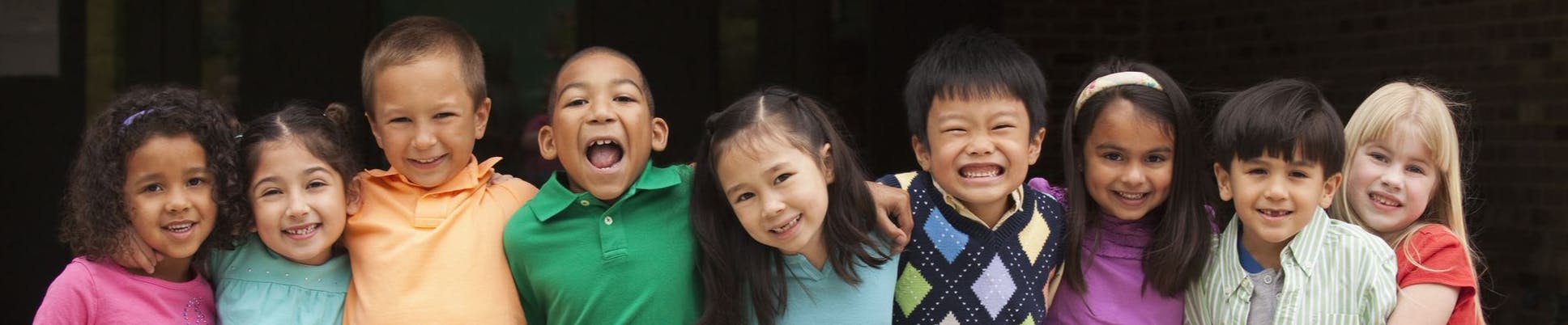 Children standing in a row with their arms around each other with huge smiles