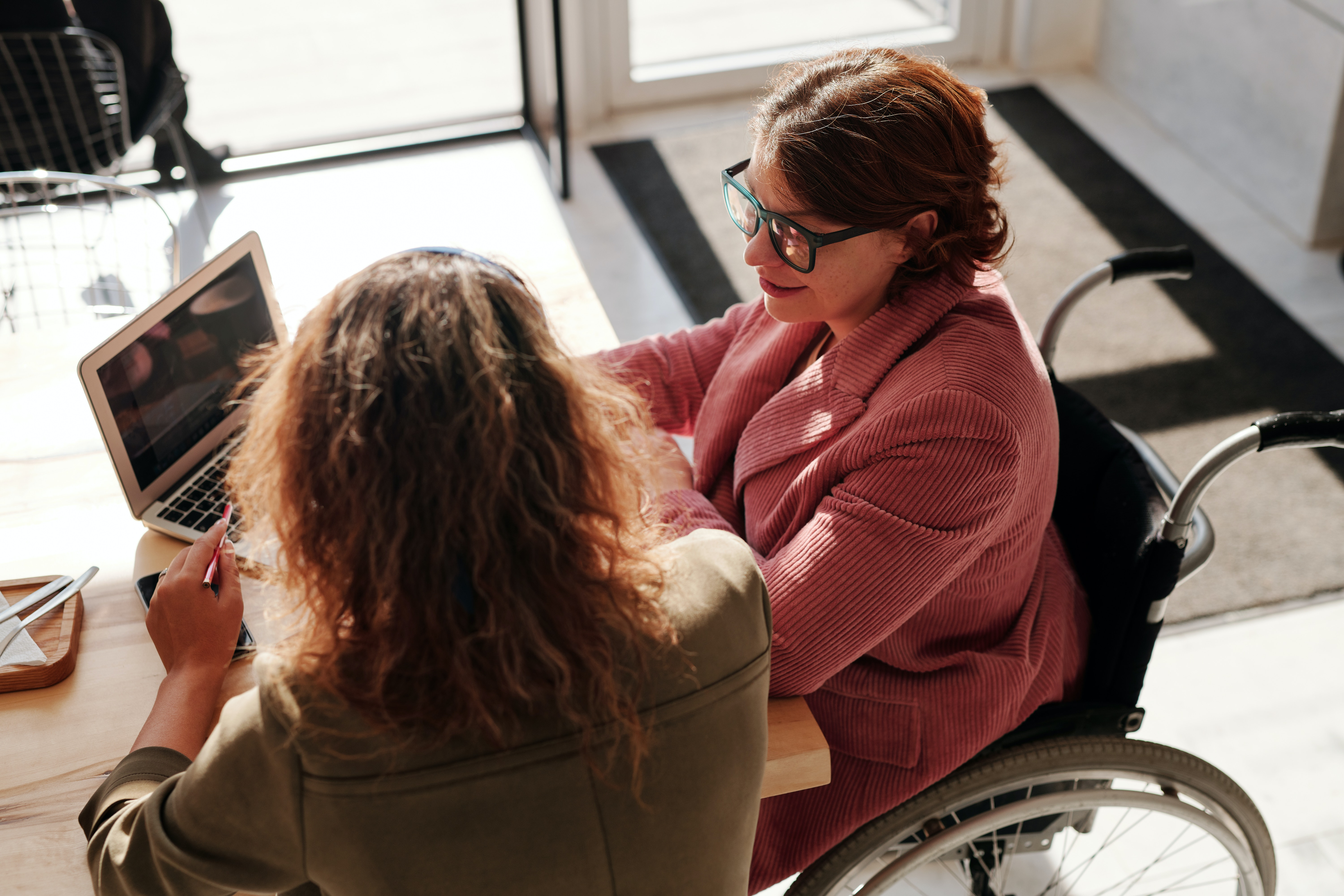 Woman in wheelchair with laptop talks to another