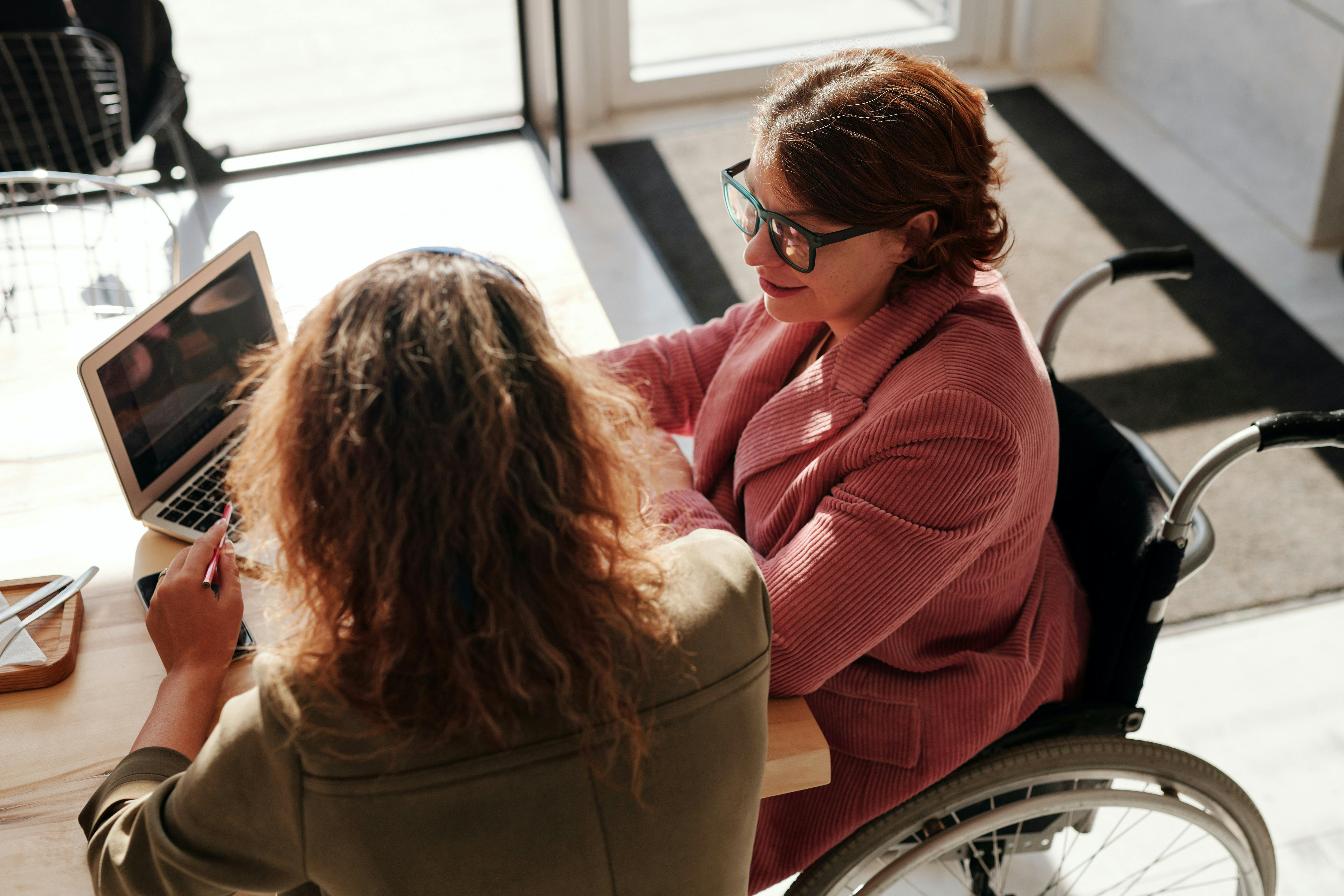 Woman in wheelchair with laptop talks to another