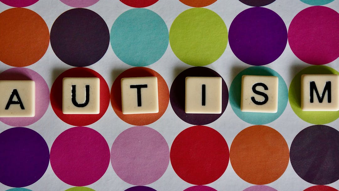 An image of Scrabble tiles spelling out the word autism on a background of multi-coloured polka dots.