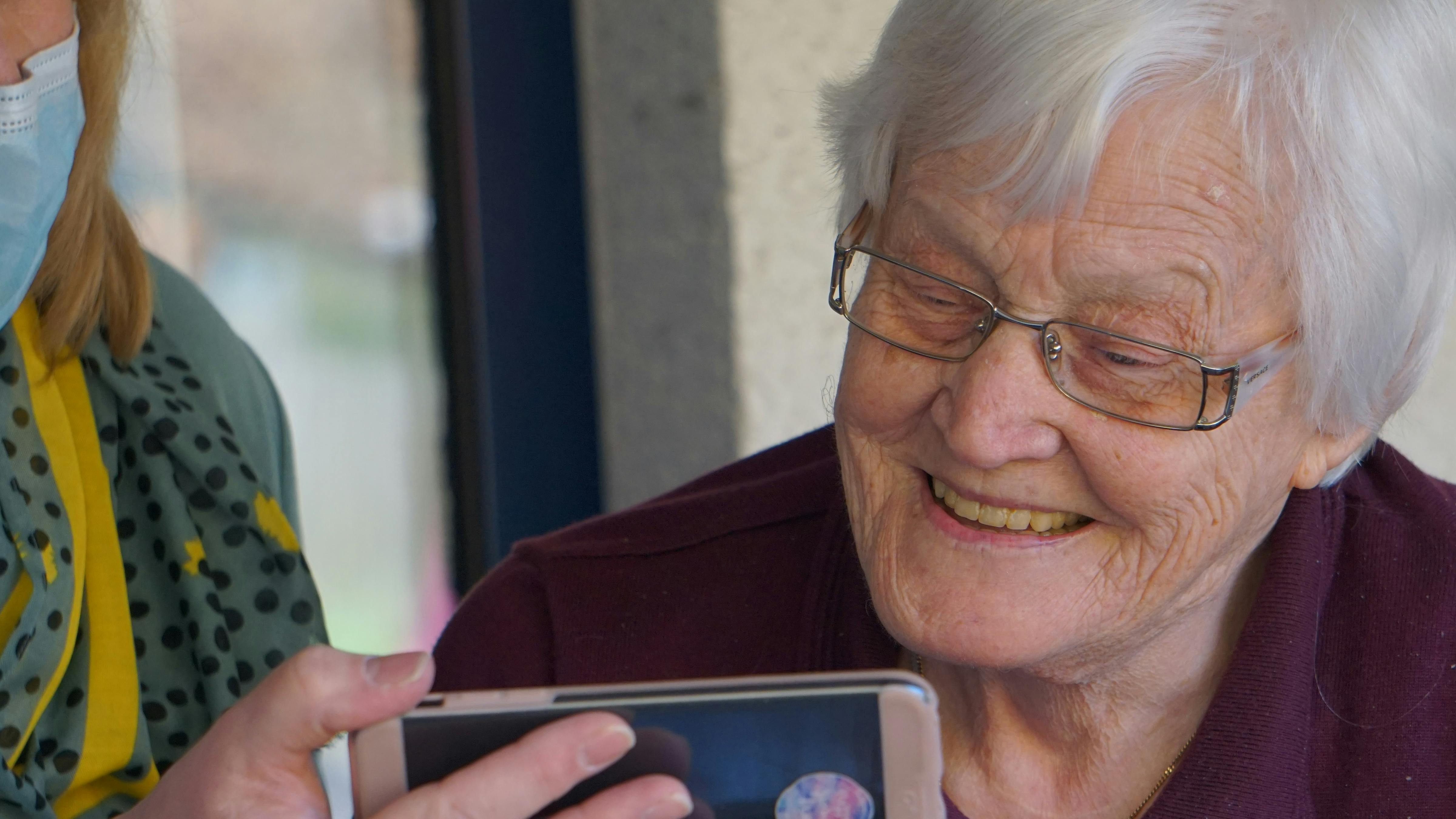 Carer supporting older woman with mobile phone.