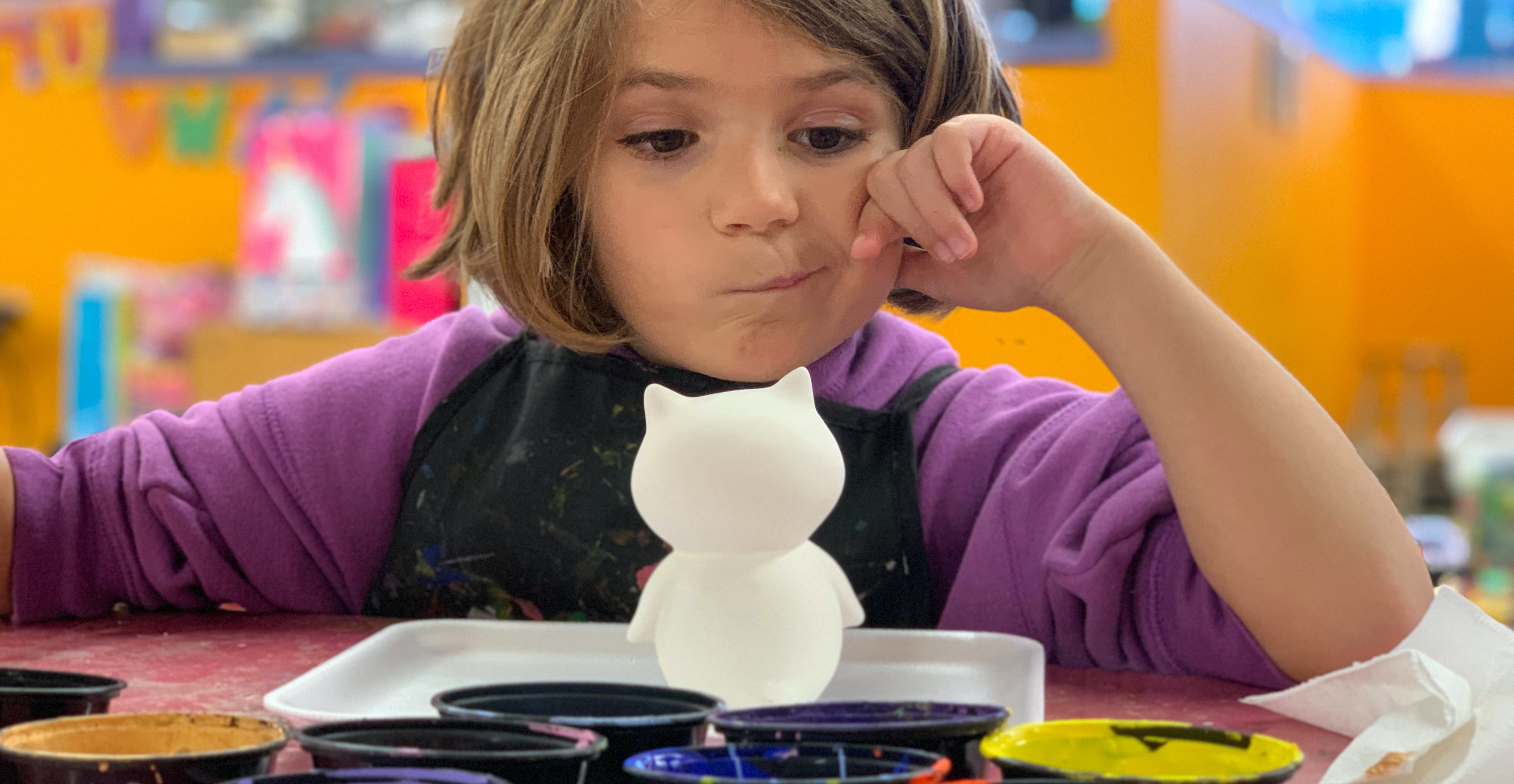 A young girl with brown hair and a purple top making a painted owl figure