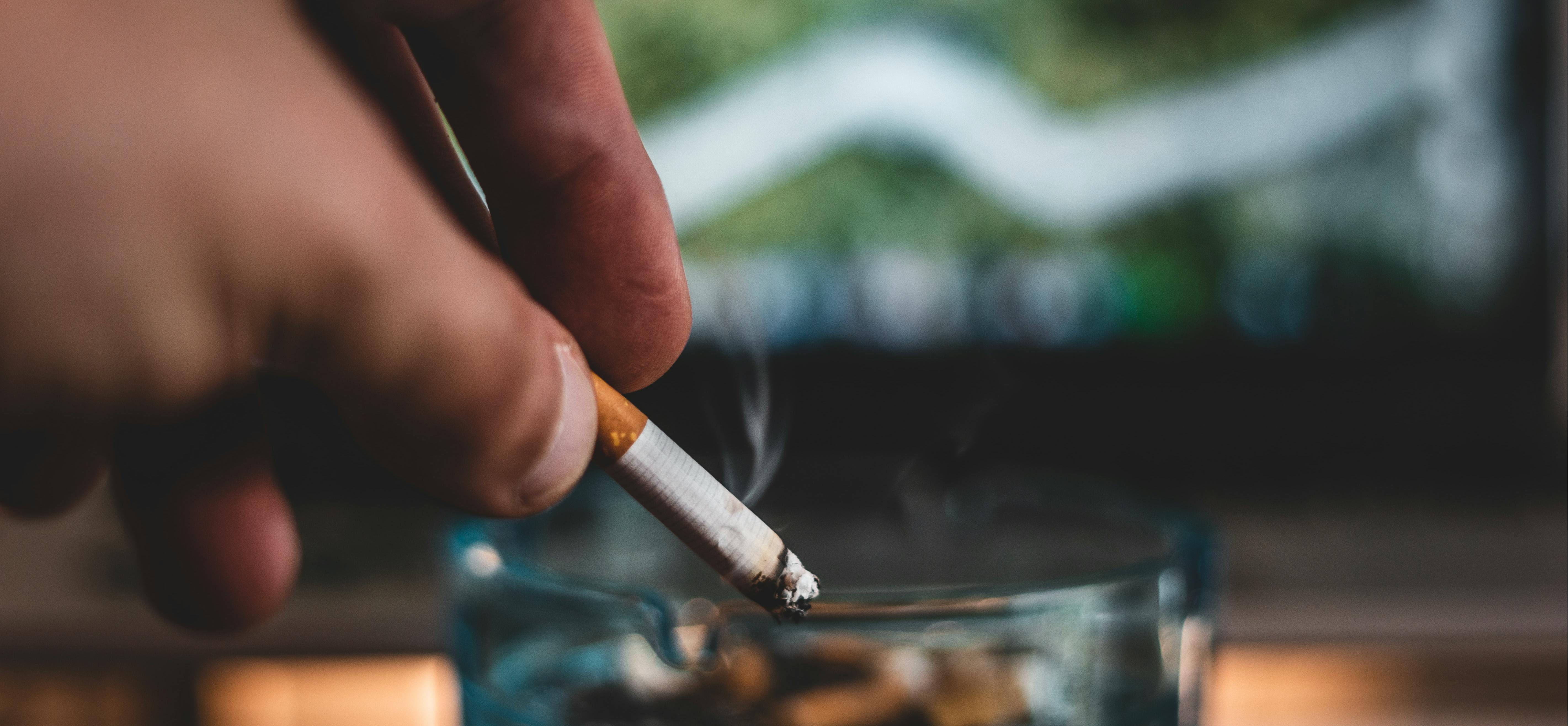 Close up of a hand stubbing out a cigarette into a glass ashtray