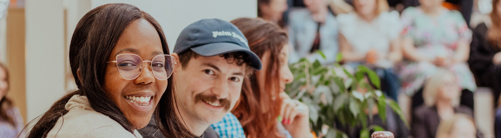 A man and a woman are looking to their right and smiling. In the background, another woman is looking ahead of her. 