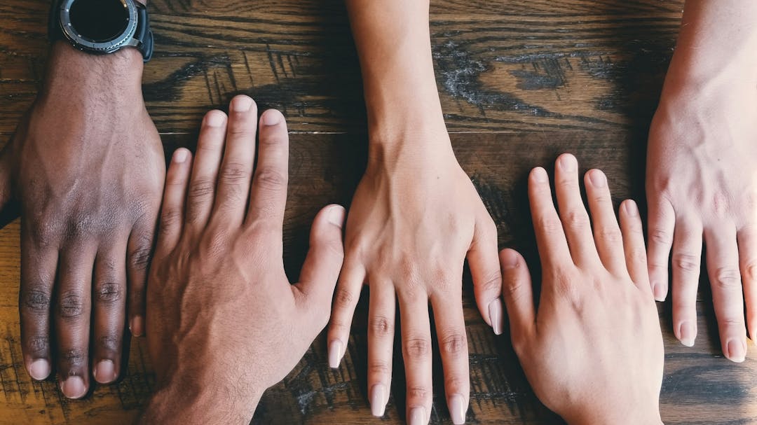 five hands in a row with palms flat on a table