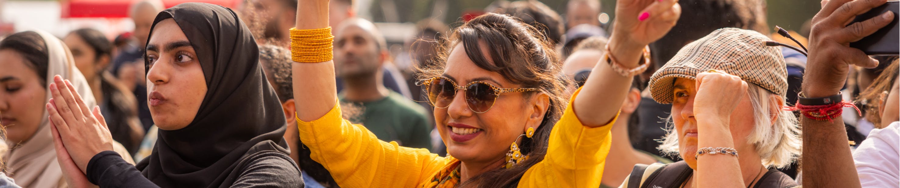 A happy crowd, with a woman in yellow smiling and waving her arms, and a woman in a black hijab clapping