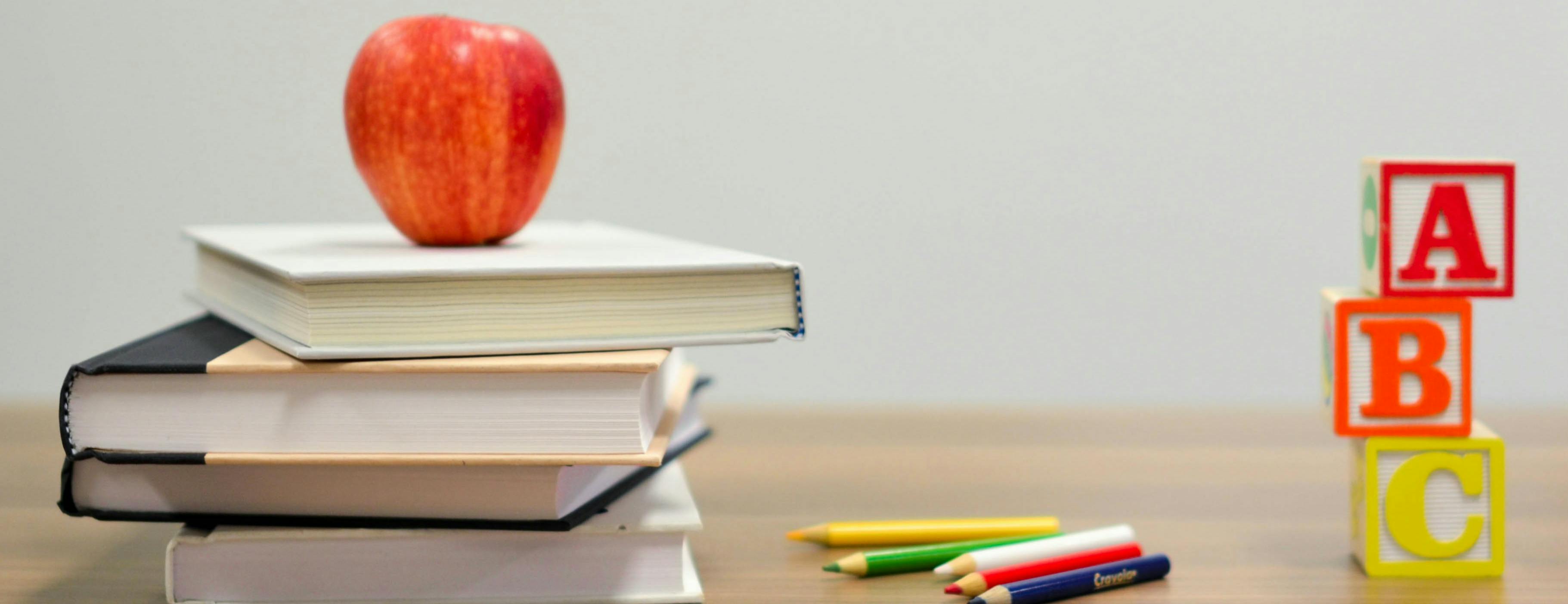 Apple on top of books next to coloured pencils and building blocks