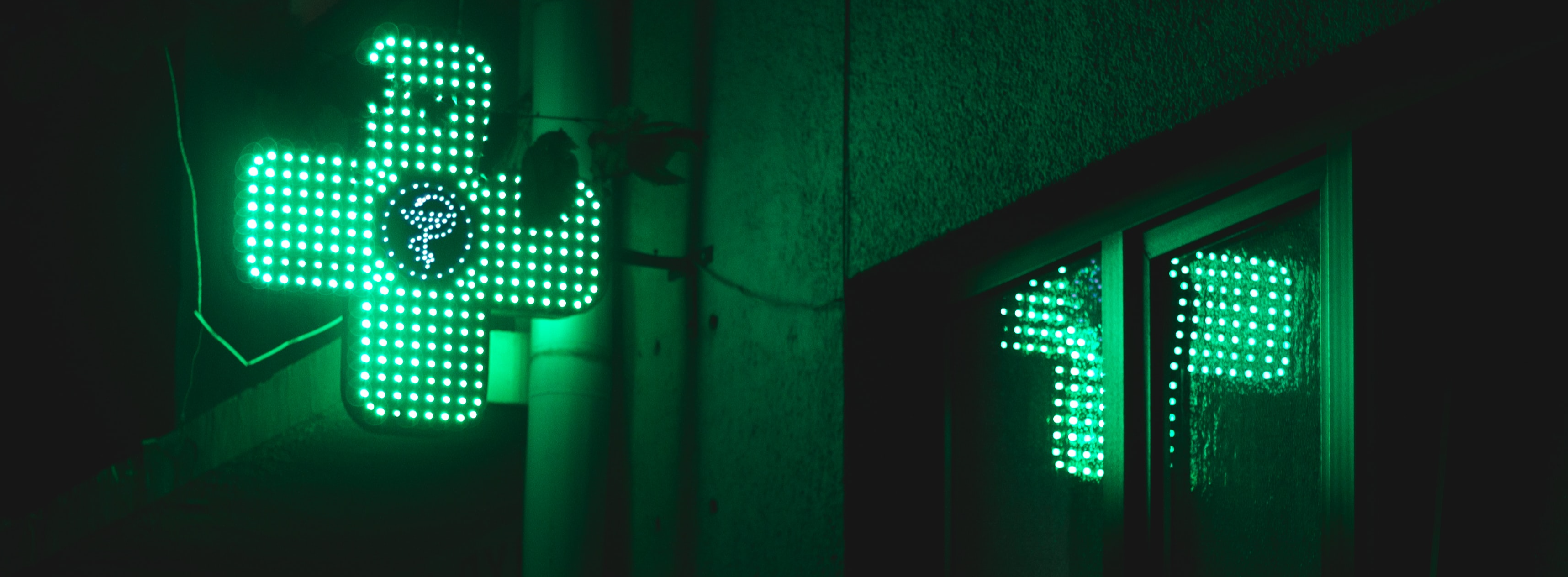 Neon green cross pharmacy sign on the side of a building in the dark