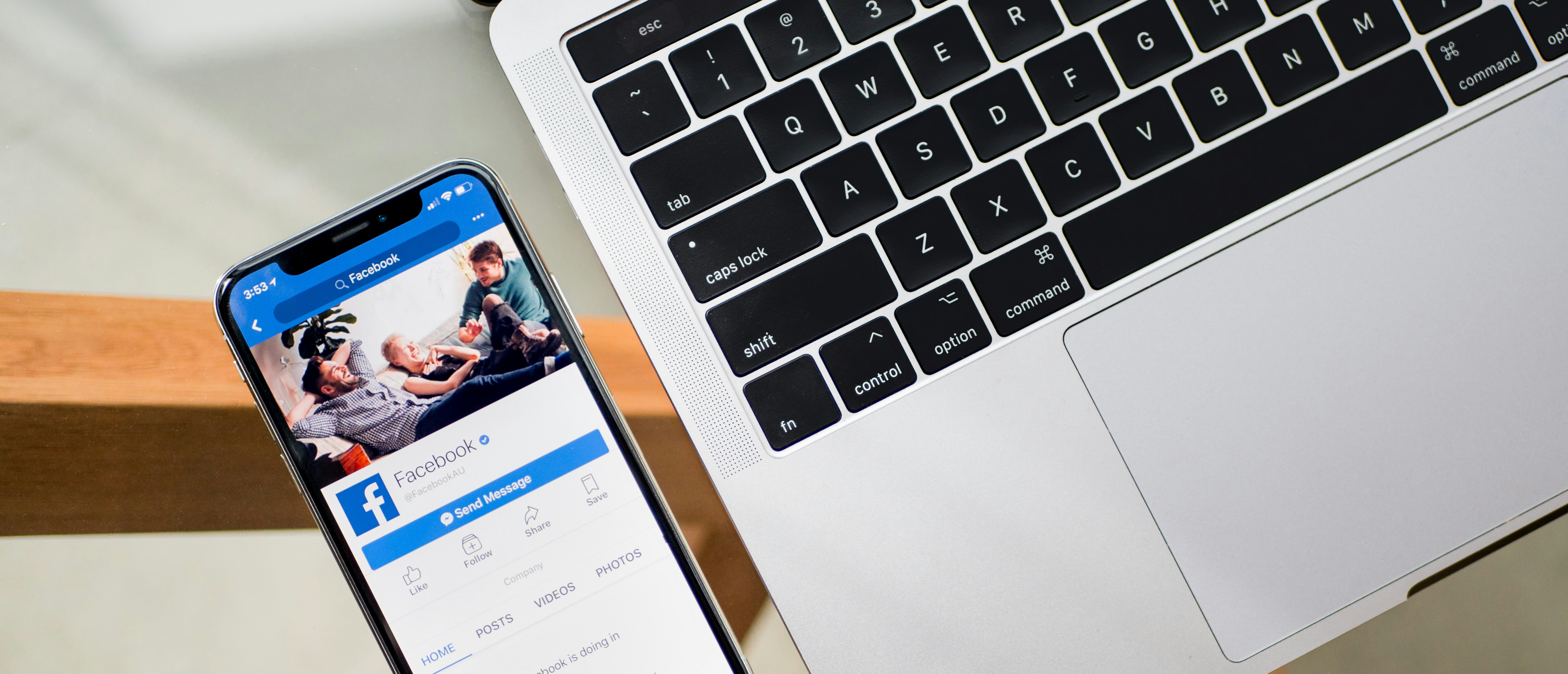 Close up of a mobile phone, with the Facebook app on the screen, next to a laptop