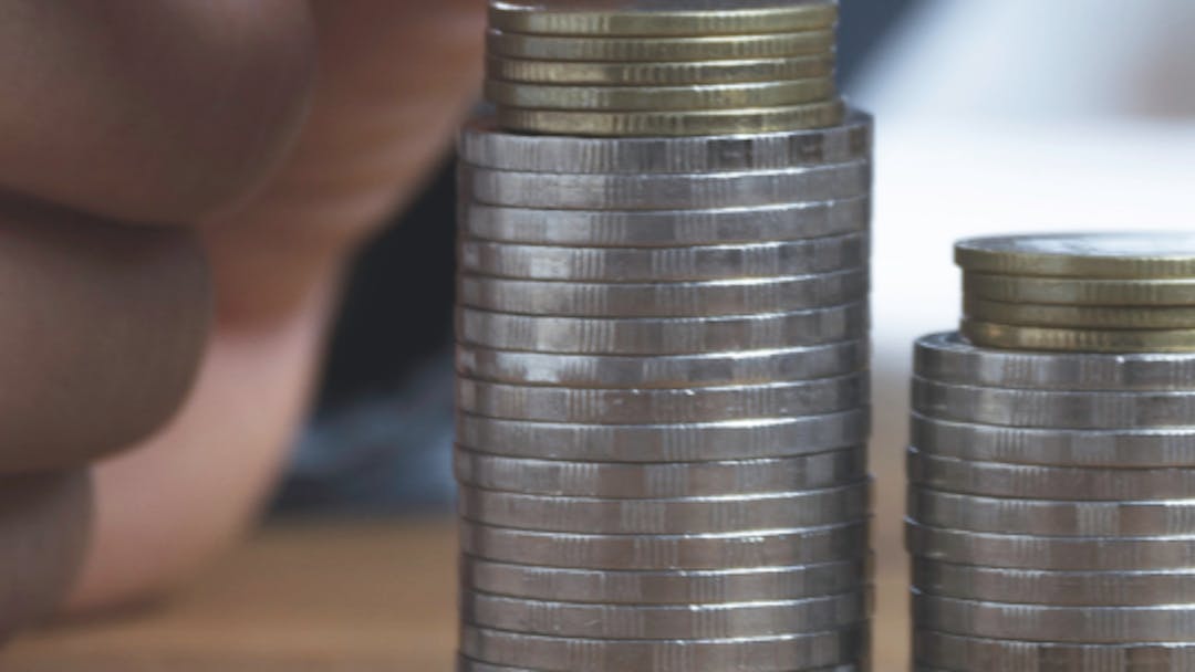 Close up of a hand placing a coin on a small stack of coins