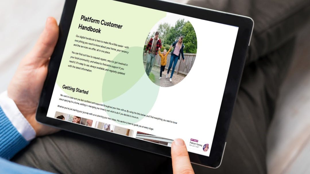 Close up photograph of a person sitting on a timber floor accessing a tablet screen showing Platform Customer Handbook 