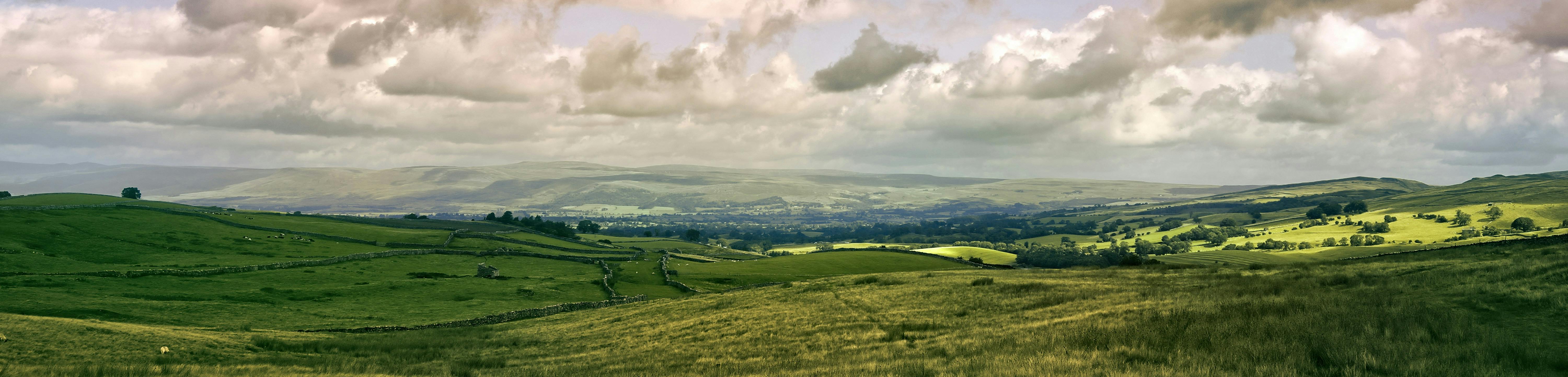 View of Cumbrian fells, a blue sky with some clouds, rolling hills and residential dwellings in the distance 
