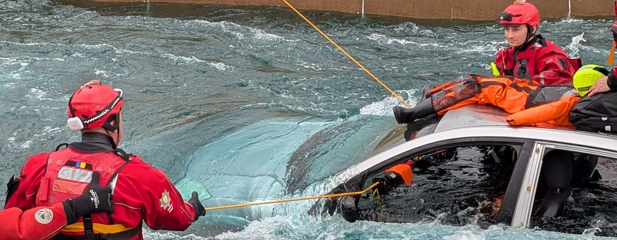 An image depicting a water rescue involving the rescue of a car in floods by three fire officers 