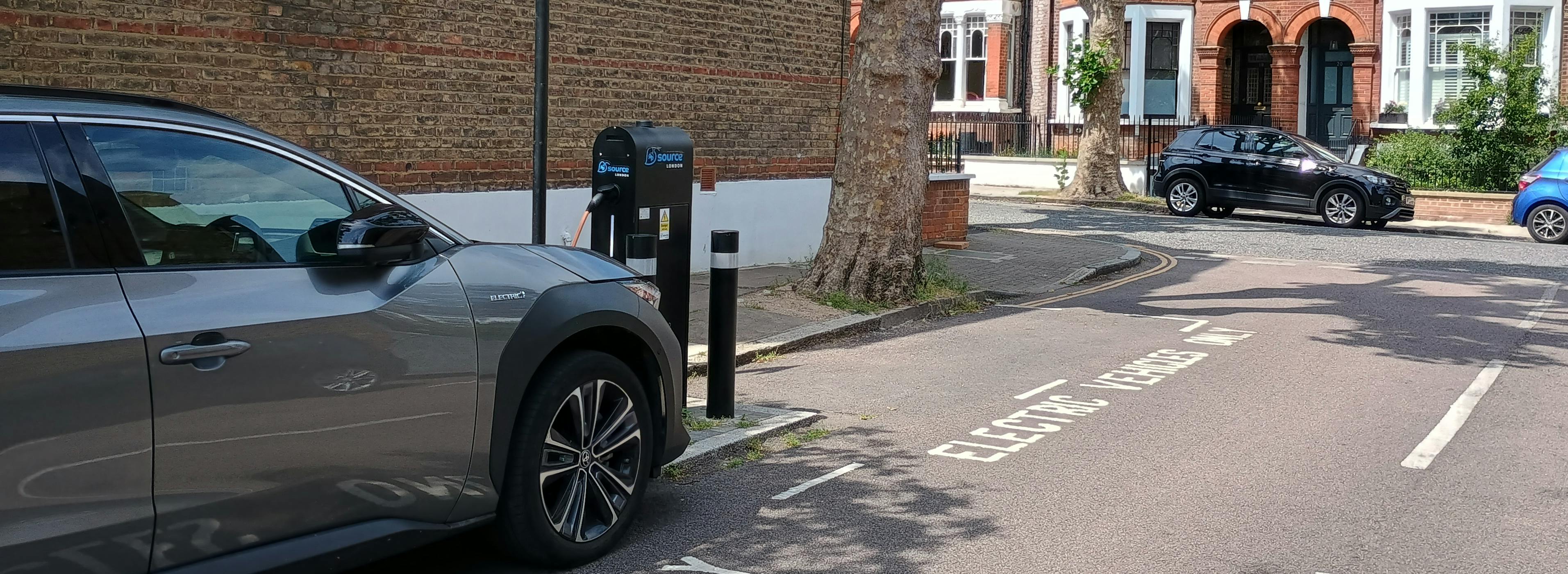 Lamp column electric vehicle charging point next to a parked car plugged in to the charging point.