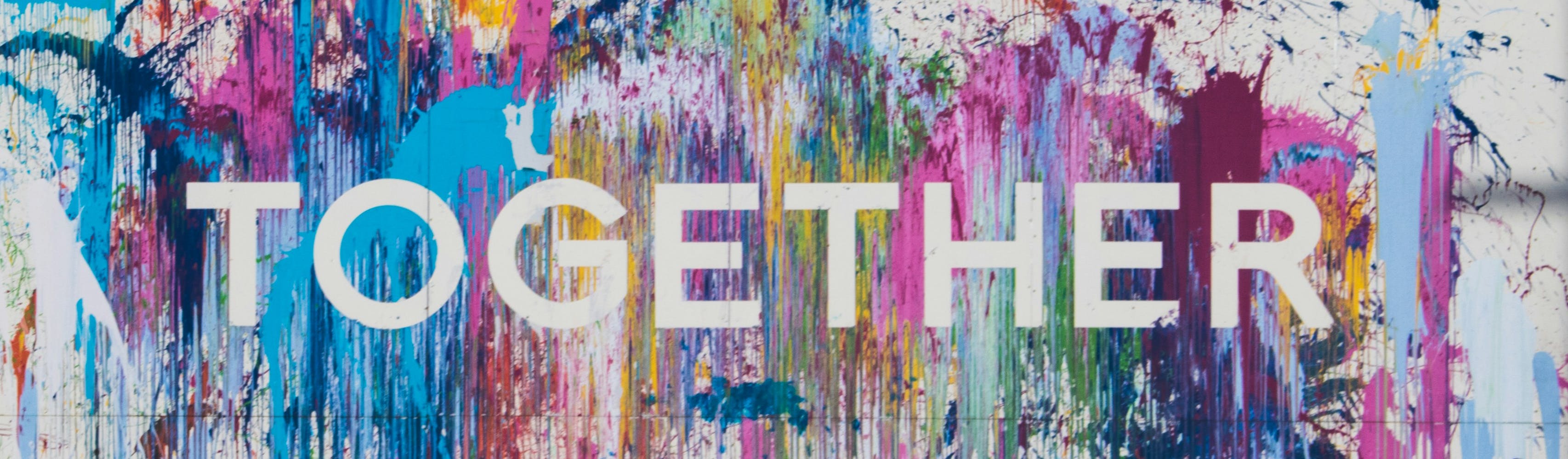 A white wall with colourful splashes of paint, with the word "Together" in the middle