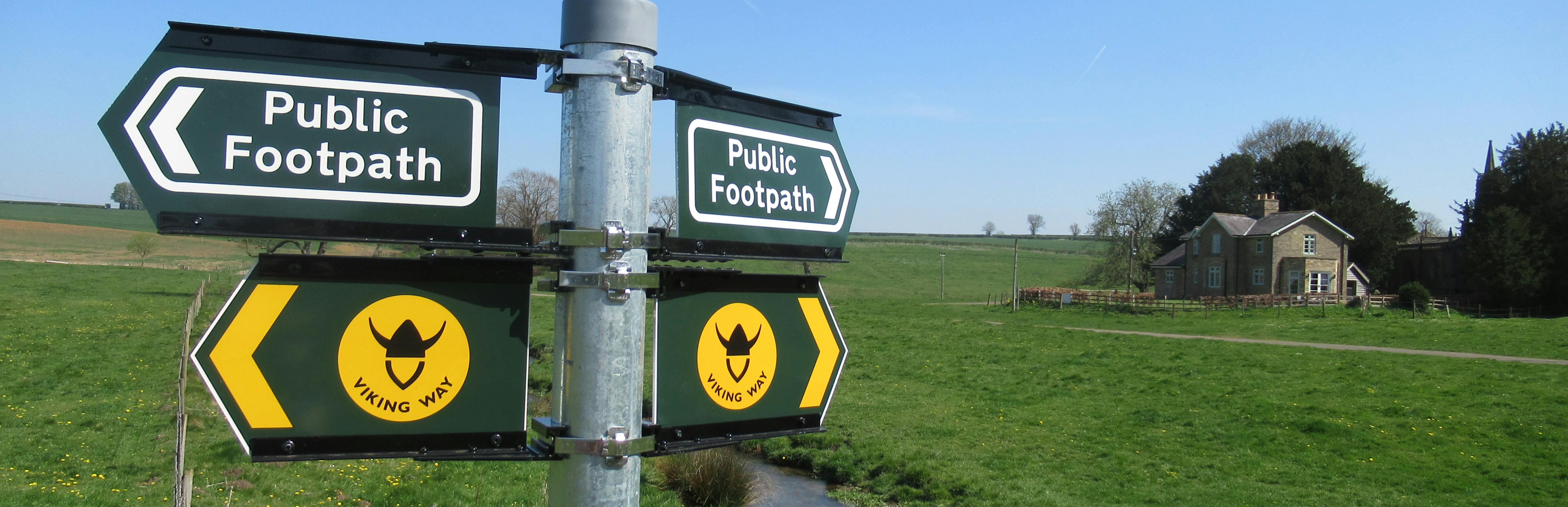 Image of walk signage by brook and a cottage in a green space