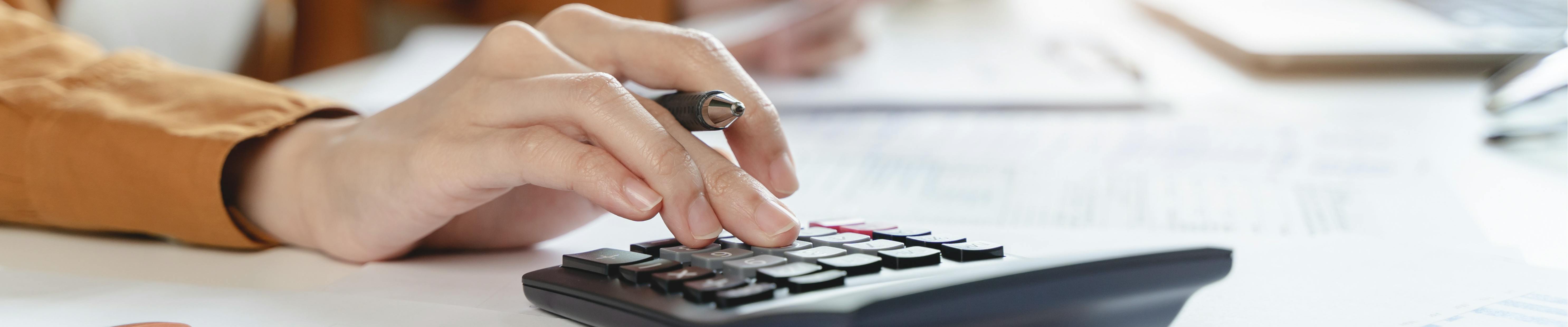 Close up of a hand holding a pen and using a calculator