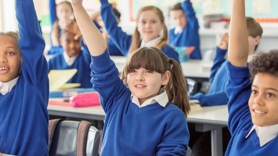 A group of primary school children raising their hands and smiling