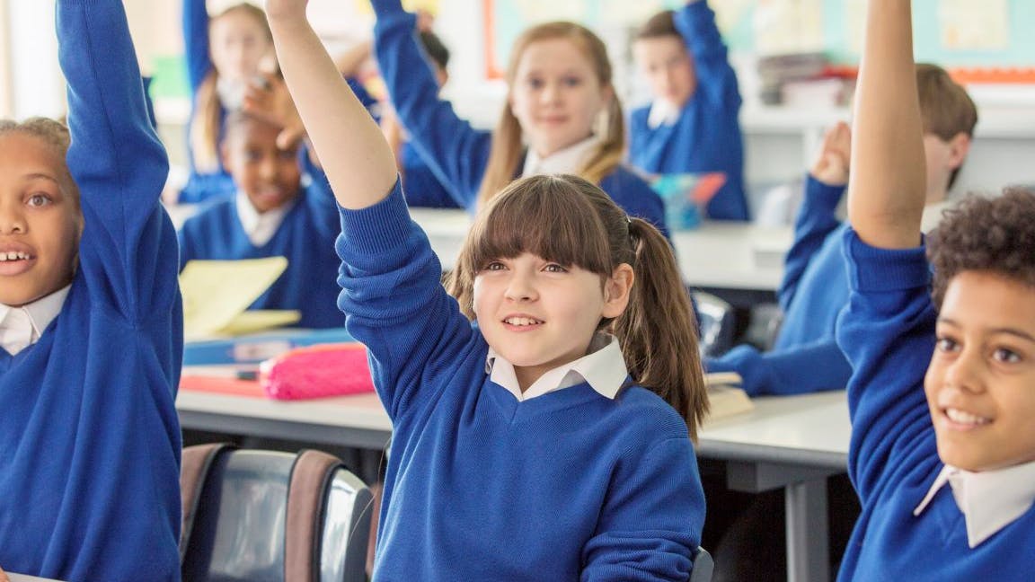 A group of primary school children raising their hands and smiling