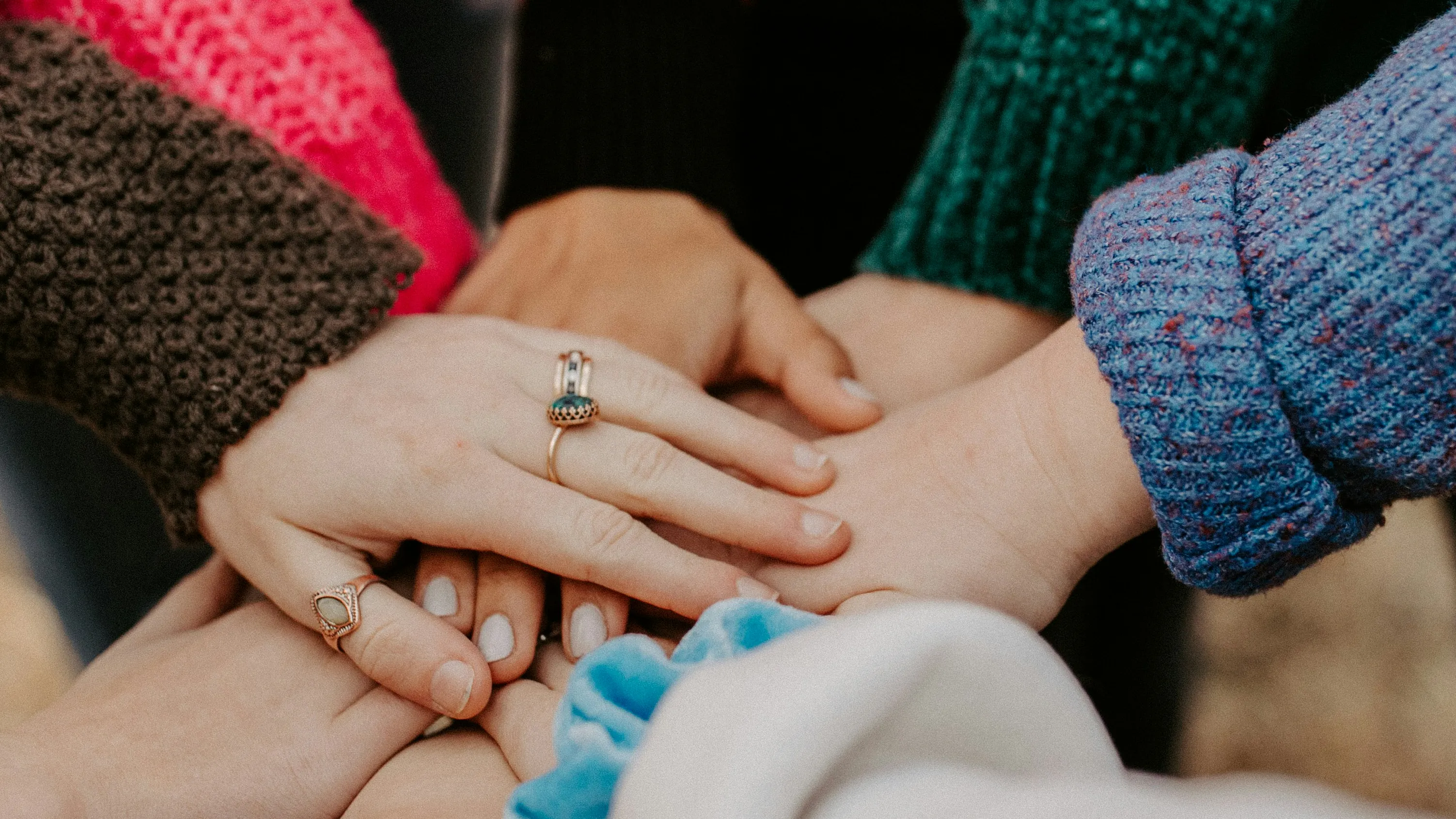 8 hands placed together in the centre of the frame, to indicate Teamwork/working together.