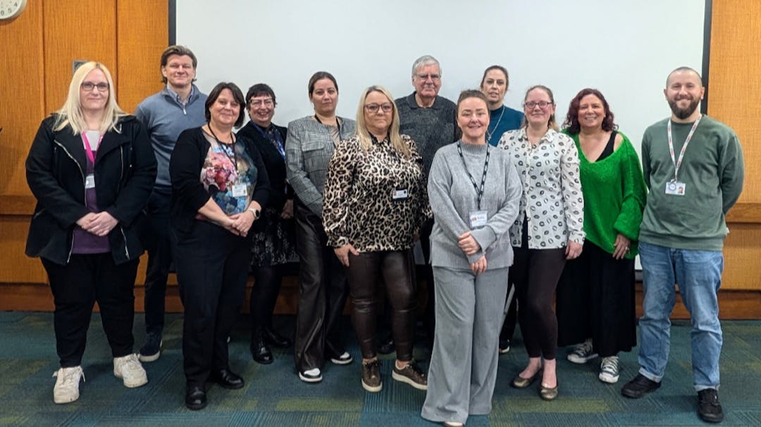 12 members of the SEND Network smiling at the camera and standing against a large white board.