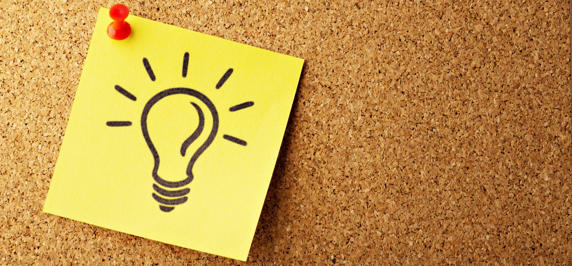 brown corkboard with a yellow note which has a bright light bulb drawn on it