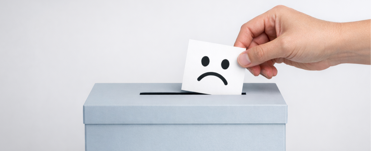 A hand dropping a card with a sad smiley face into a grey feedback box