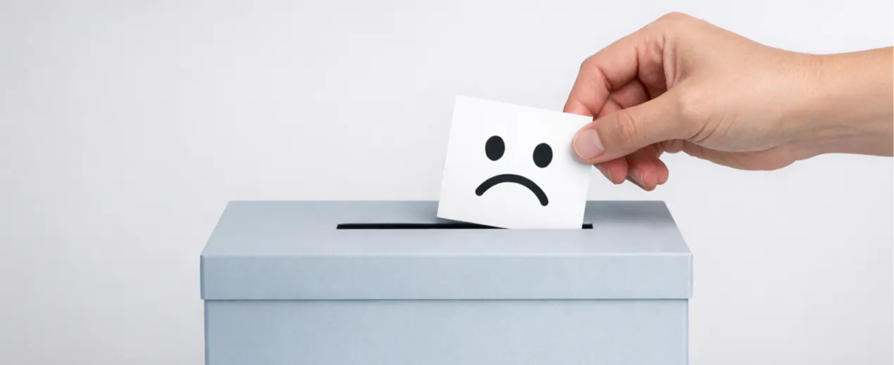 A hand dropping a card with a sad smiley face into a grey feedback box