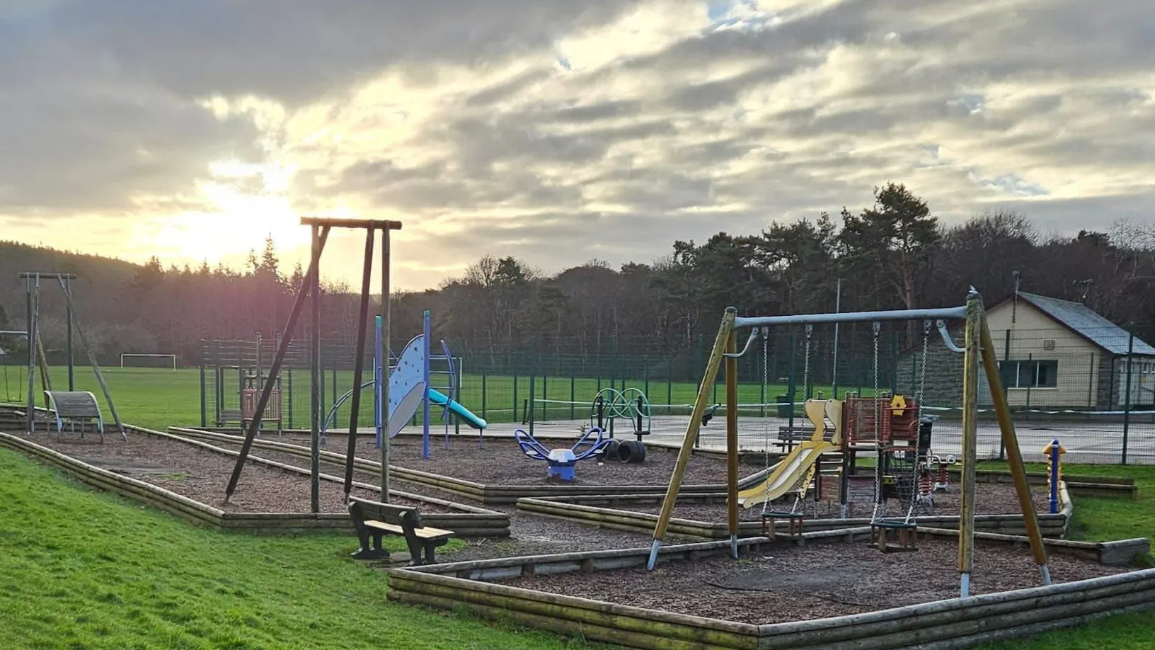 A picture showing a children's play area with equipment such as swings, a climbing frame and a slide 
