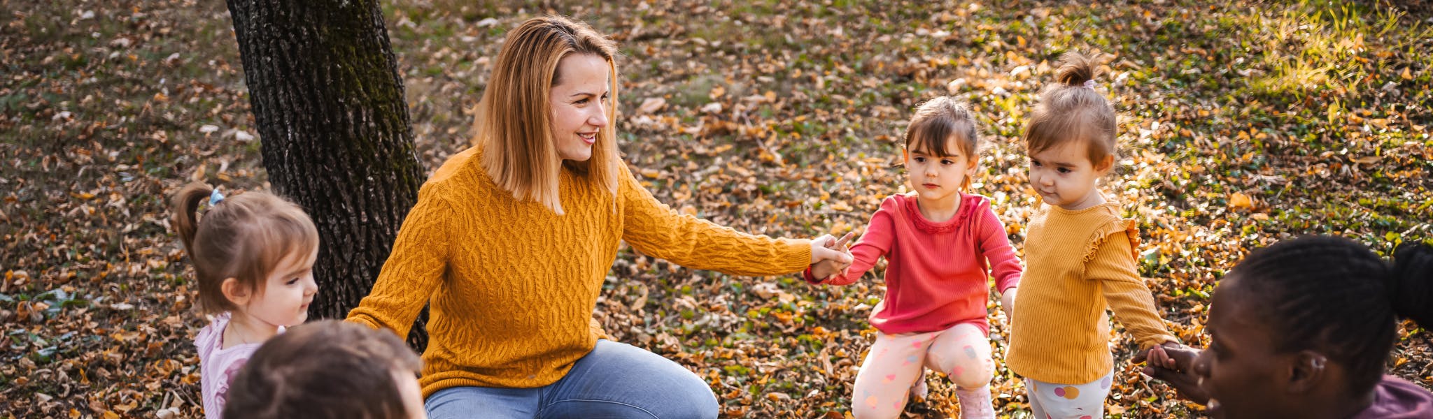An image of a group of children and one adult in a circle holding their hands
