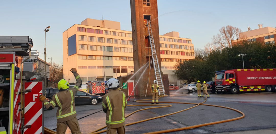 fire fighter using hand signal at rear of appliance, ladder in to the third floor of the building, with multiple hose jets