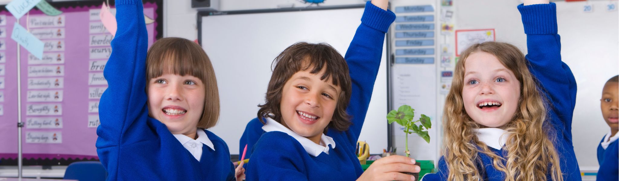 An image of 3 children raising their hands in a classroom