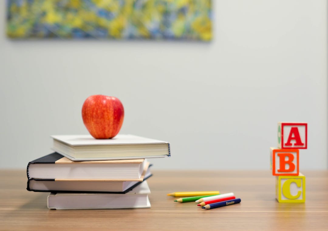 Table with 4 books, an apple, colouring pencils and ABC wooden blocks