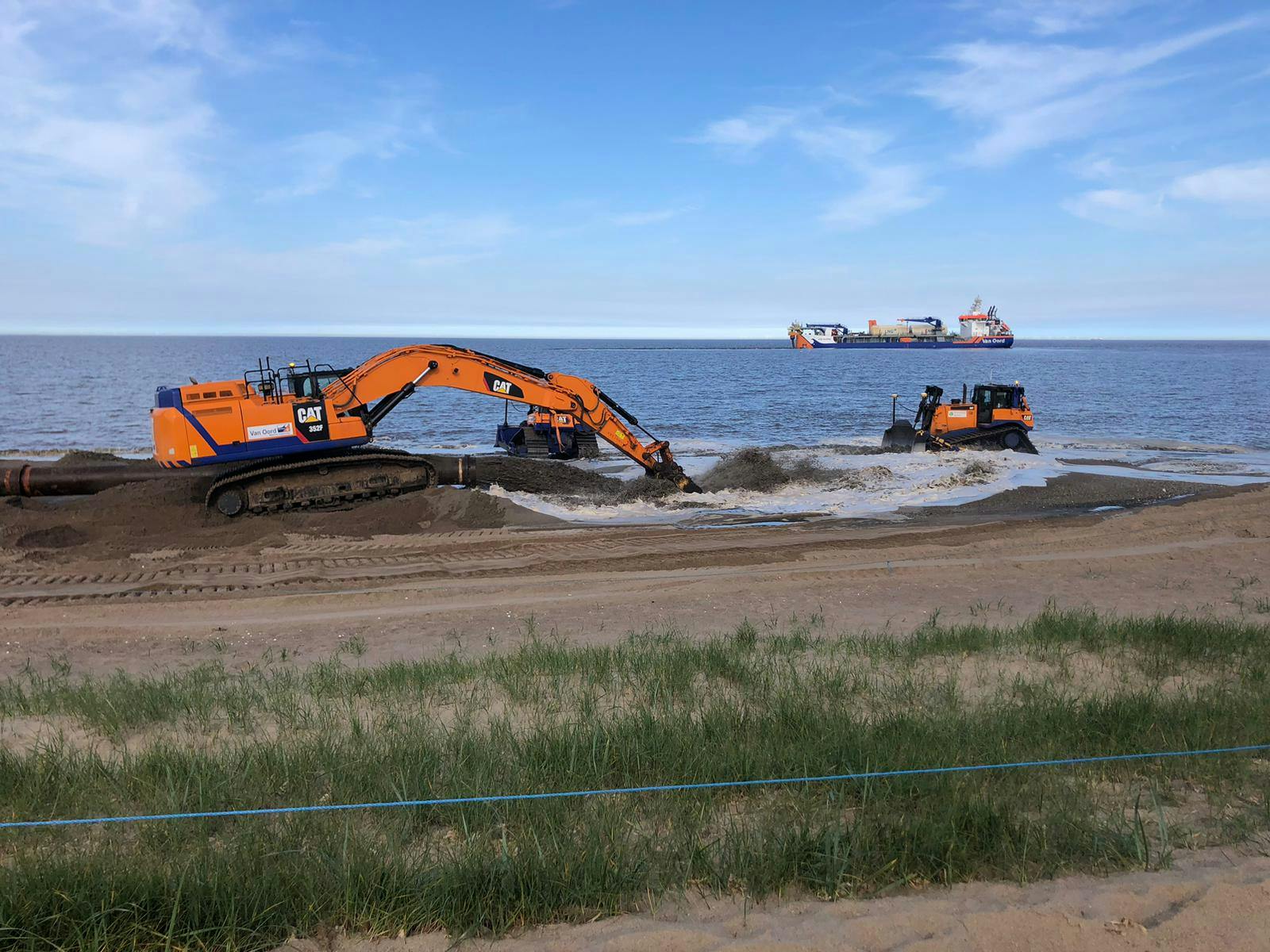 Machinery moves the sand on the beach whilst sand is pumped through the sinkerline from the dredger on the horizon