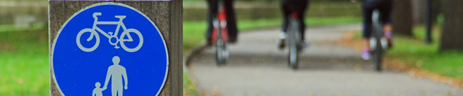 Cycle/Walking Path blue sign on a wooden post with three cyclists on the path in the background