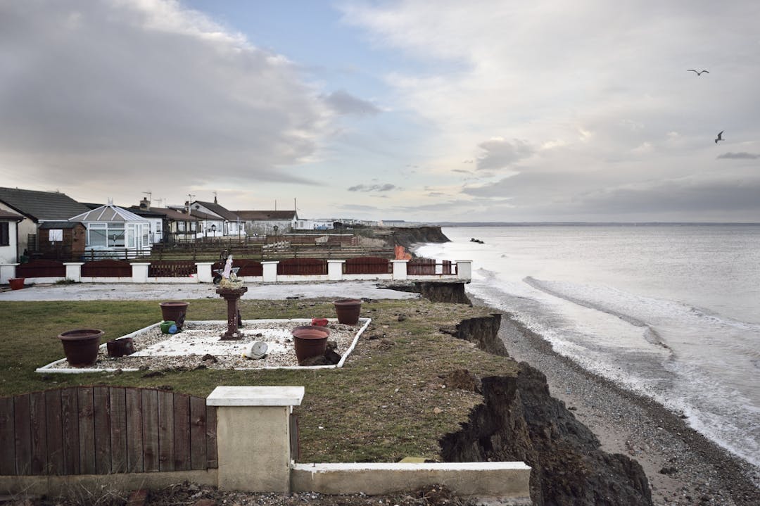 A photograph of the sea and an eroding cliff edge with residential gardens back at the cliff edge.