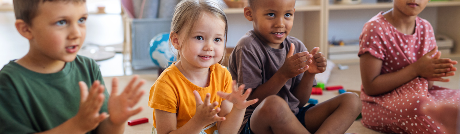 Group of children sitting on the floor clapping.