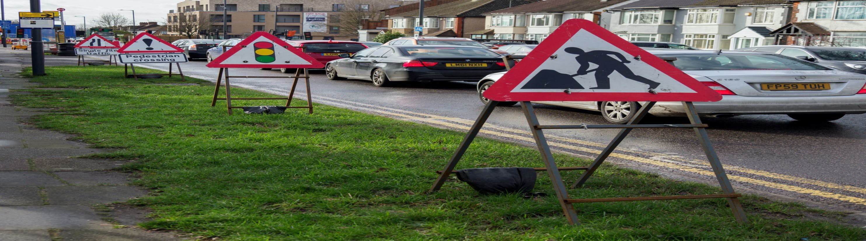 Photo of queuing cars behind various traffic signs. 