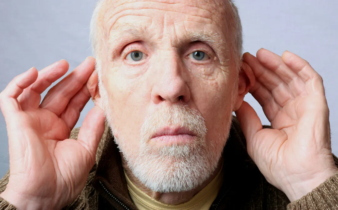 A man holding his hands up to his ears indicating he is trying to hear what is being said