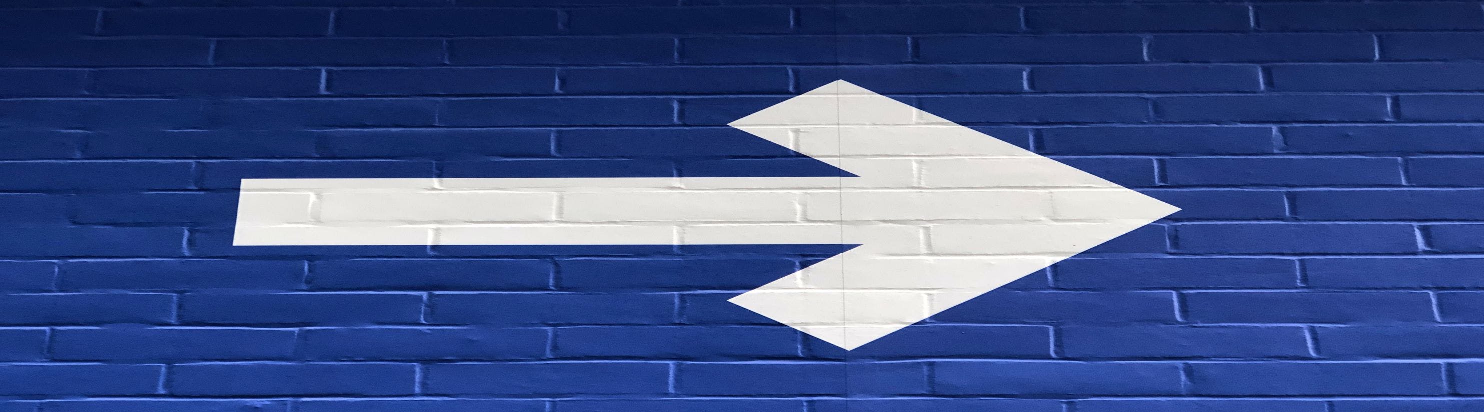 Photo of white arrow on blue brick wall.