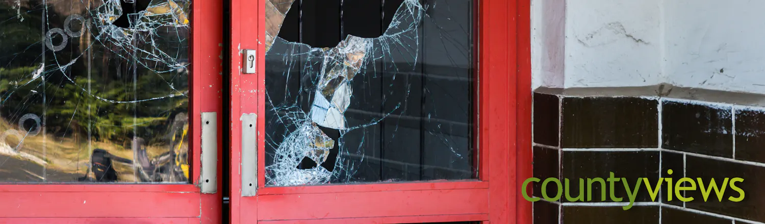 Picture of a broken window in a shop door with County Views logo in the corner