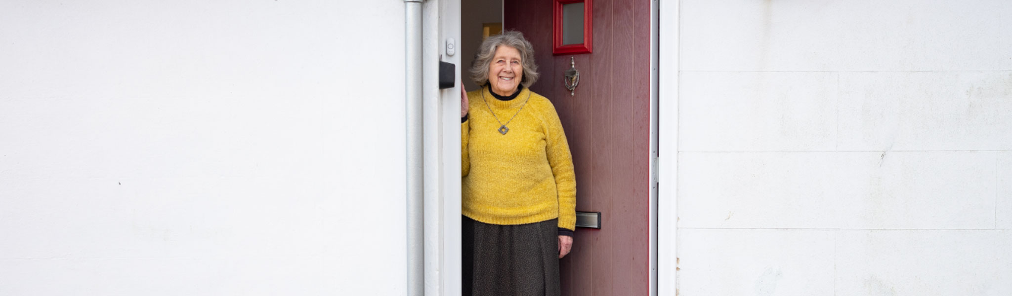 Older lady looking out of her front door of her white bungalow