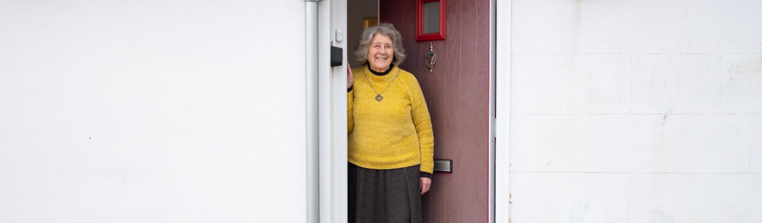 Older lady looking out of her front door of her white bungalow