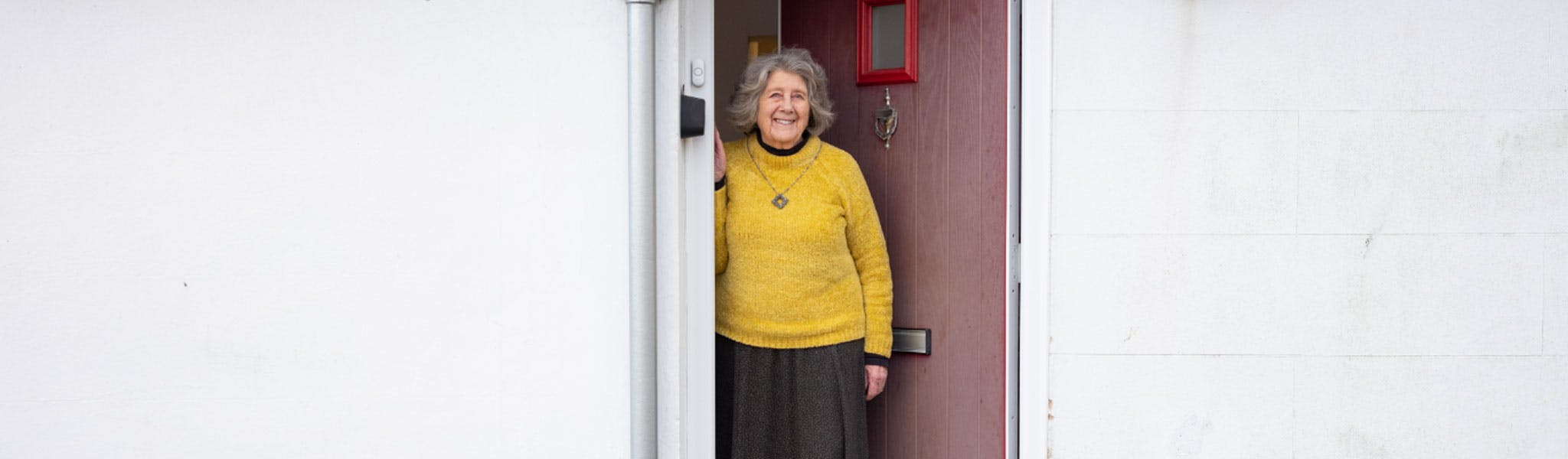 Older lady looking out of her front door of her white bungalow
